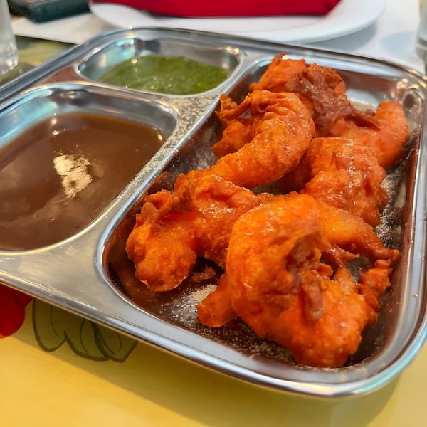 Himalayan Kitchen's chicken pakora, a fried Indian appetizer, served with two dipping sauces on a metal tray.