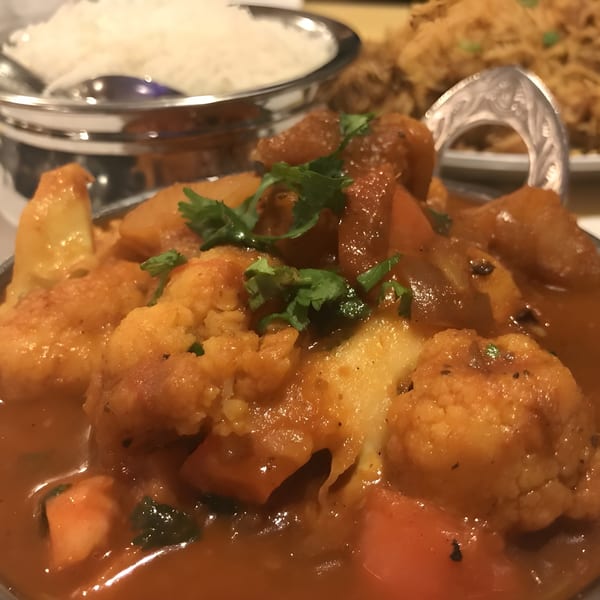 Close-up of Indian vegetable curry with cauliflower, potatoes, and cilantro, with rice in the background.